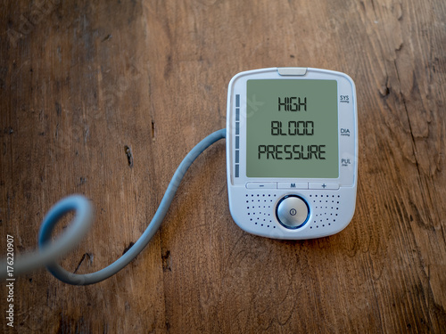 Digital Blood pressure gauge show Hypertension or High Blood Pressure on screen. Text on monitor. Wood background.