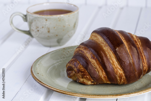 Fresh chocolate croissants and tea cup for breakfast on white wooden vintage table