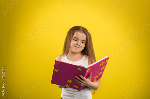 Concept - education. Girl reading a book in a pink cover, shooting in the studio on an isolated yellow background