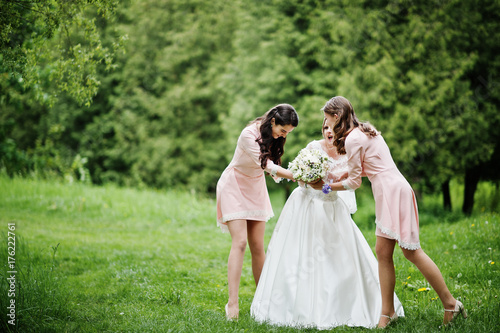 Attractive bride posing and having fun with two her bridesmaids in the park on a sunny spring wedding day.