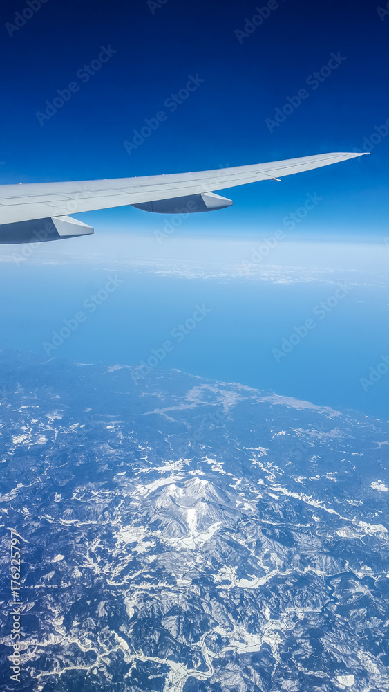 Naklejka premium Aerial view from airplane window over Japan with airplane's wing,mountains covered snow and blue sky background.
