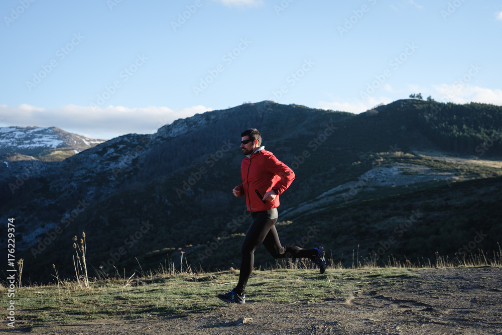 Sporty man running cross country outdoor on the mountain. Athlete training and exercising in late winter.
