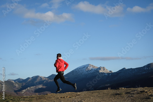 Sporty man running cross country outdoor on the mountain. Athlete training and exercising in late winter.