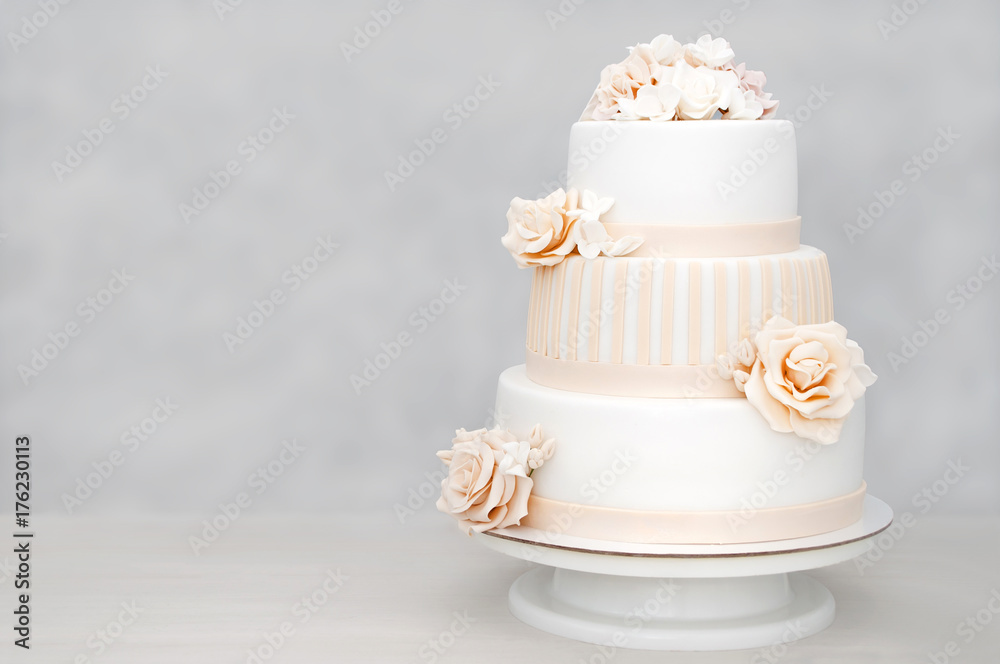 Ταπετσαρία Three-tiered white wedding cake decorated with flowers from mastic on a white wooden table