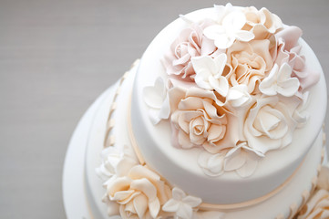 Three-tiered white wedding cake decorated with flowers from mastic on a white wooden table. Picture for a menu or a confectionery catalog. Top view.