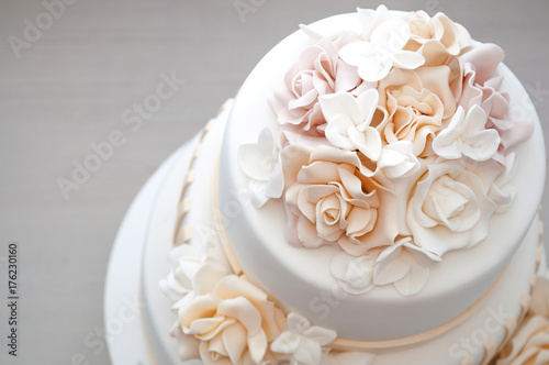 Three-tiered white wedding cake decorated with flowers from mastic on a white wooden table. Picture for a menu or a confectionery catalog. Top view.