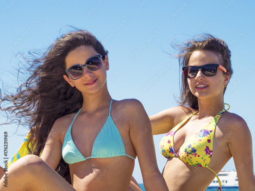 Portrait of two beautiful young women sitting by sea on pier enjoying summer sunny day Fun, recreation - concept.