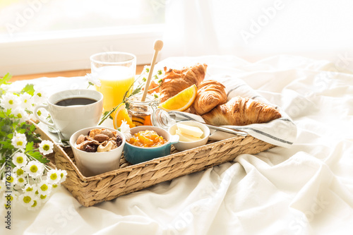 Wicker tray with continental breakfast on white bed sheets photo