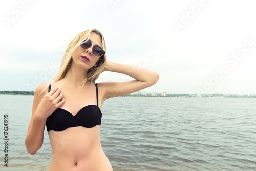 Beautiful girl in heart-shaped sunglasses and a gorgeous body posing on sandy beach. Concept of dreamy memories from trips