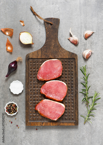 Uncooked fresh steak for roasting with spices and herbs on a rustic wooden board. Overhead view.