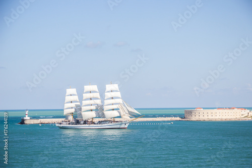 old historical tall ship with white sails in blue sea