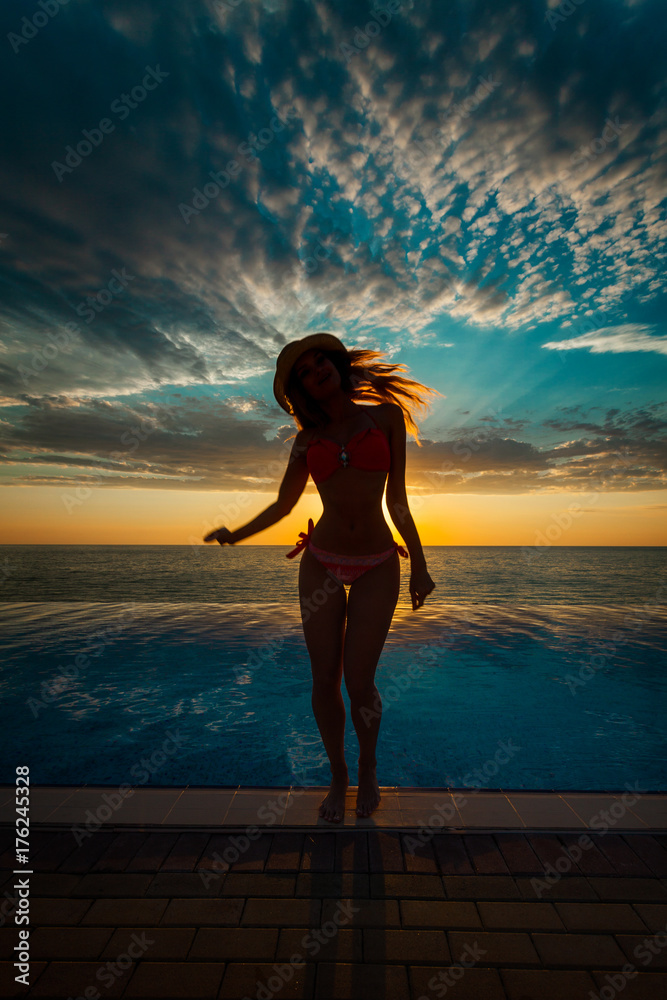 Summer Vacation. Silhouette of beauty dancing woman on sunset near the pool with ocean view.