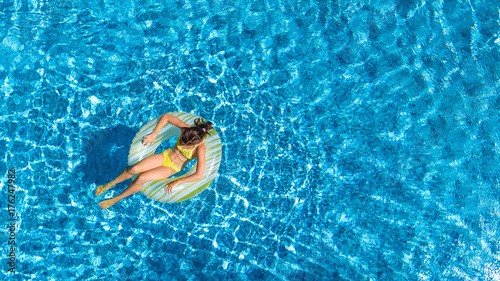 Aerial view of girl in swimming pool from above, kid swim on inflatable ring donut and has fun in water on family vacation 