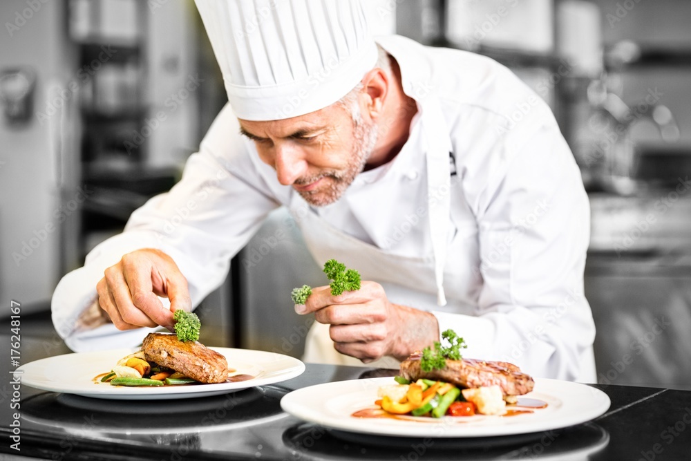 Concentrated male chef garnishing food in kitchen Concentrated male chef garnishing food in kitchen