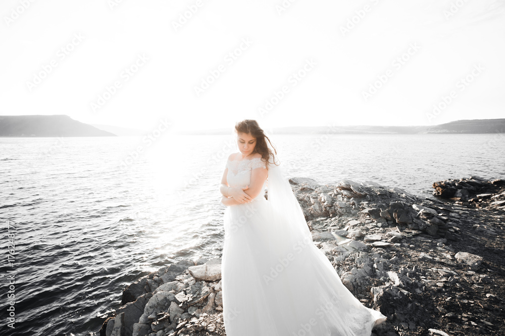 Pretty lady, bride posing in a wedding dress near sea on sunset Pretty lady, bride posing in a wedding dress near sea on sunset