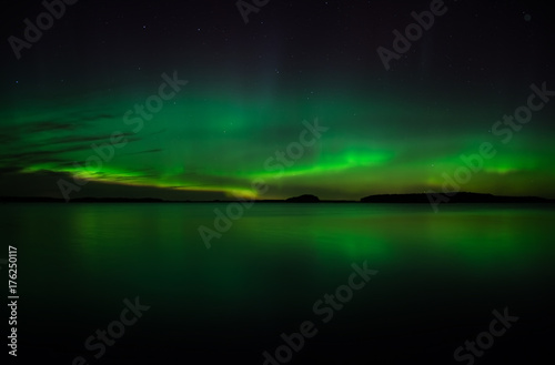 Northern lights dancing over calm lake. Farnebofjarden national park in Sweden.