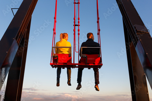 Young couple on the swing on the roof of tower at sunset time