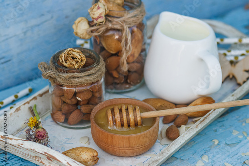 Honey in the wooden bowl, almonds and jar with milk on the wooden tray