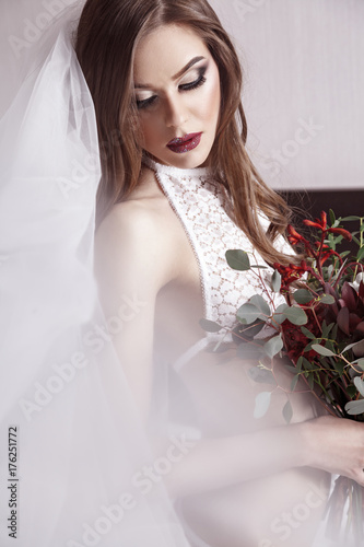 Brunette sexy lady in elegant white lingerie wearing wedding veil, looking down, holding flowers photo