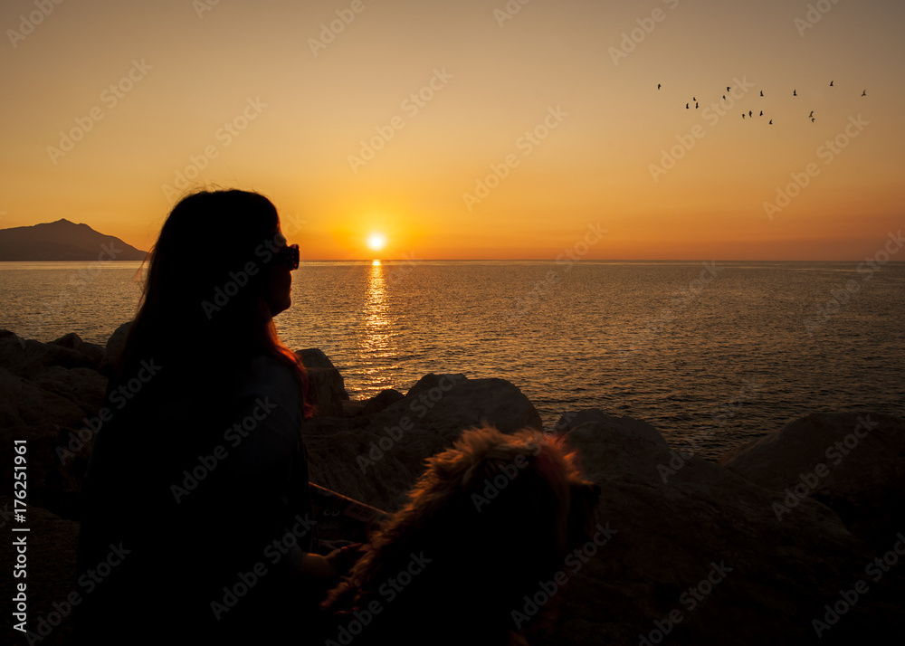 silhouette of woman and dog looking at sunset.
