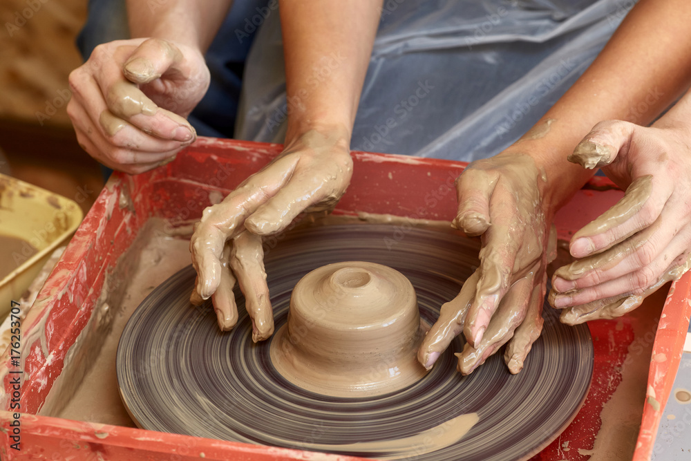 Hands of two people create pot, potter's wheel. Teaching pottery