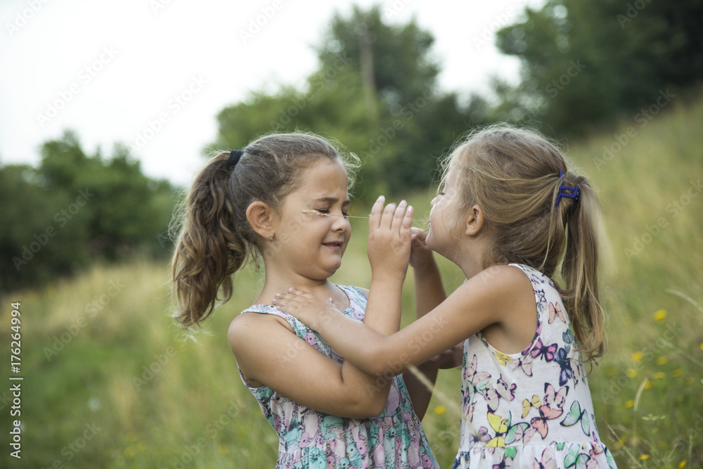 children friend girls playing whispering on flowers grass in vacations,Two adorable girls in dresses playing on the meadow