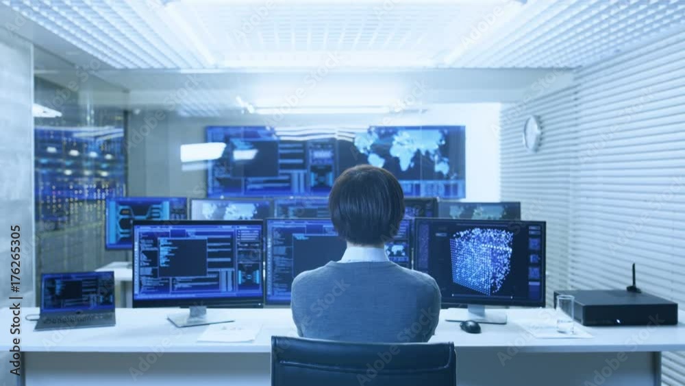 Back View of the IT Engineer Working with Multiple Monitors Showing Graphics, Functional Neural Network. He Works in a Technologically Advanced System Control Data Center.