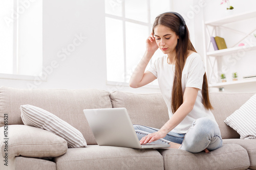 Pensive girl in headphones listening to music and using laptop