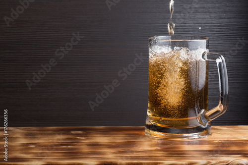 Mug of beer on wood surface. Dark background.