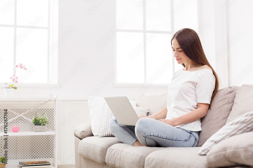 Young women using laptop sitting on sofa in white livingroom Young women using laptop sitting on sofa in white livingroom