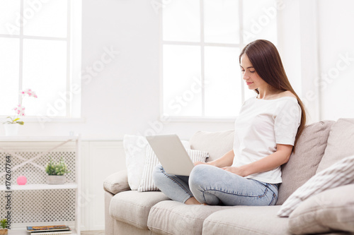 Young women using laptop sitting on sofa in white livingroom
