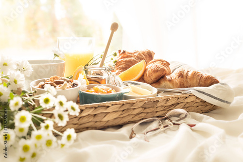 Wicker tray with continental breakfast on white bed sheets