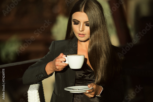 Fashion business woman is wearing black official clothes drinking coffee outdoors