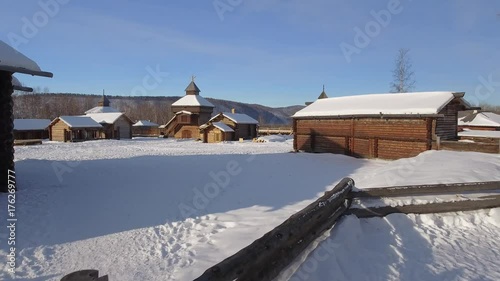 Old authentic Russian village Taltsy wooden Baikalsky tract buildings. Approach church domes roof snow Bikal. Tourist attraction. Winter frozen day. Aerial drone low gimbal cinematic  photo