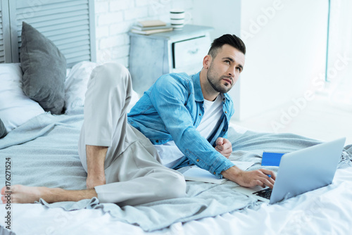 Pensive freelancer lying in bed while working from home
