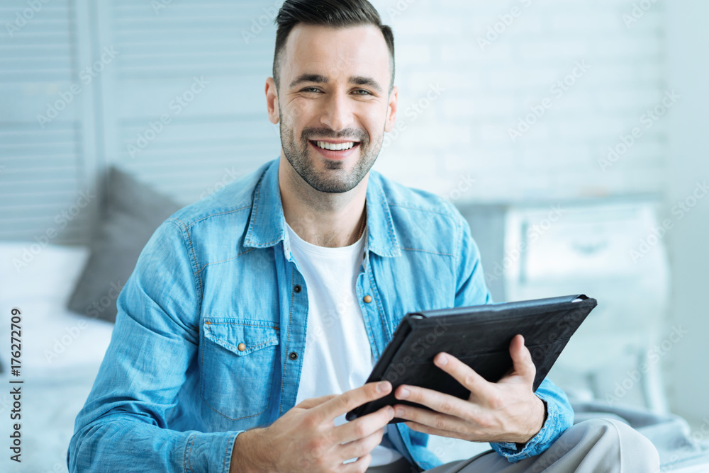 Extremely happy young man with tablet grinning broadly Extremely happy young man with tablet grinning broadly