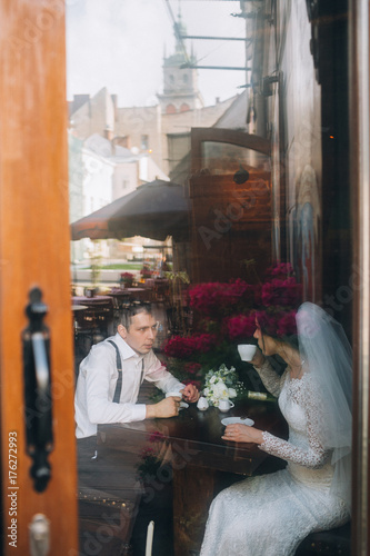 Look at wedding couple drinking coffee behind the doors in a cafe