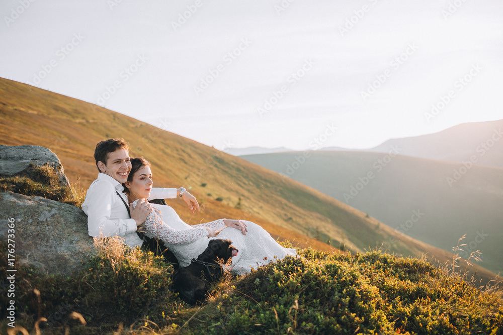 Cheerful newlyweds rest on the rocks in the rays of evening sun