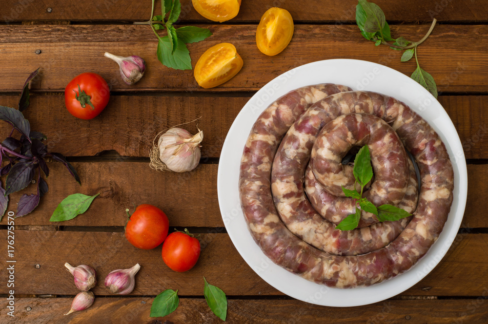 Raw fresh sausages in a white plate on a wooden background. Top view. Close-up Raw fresh sausages in a white plate on a wooden background. Top view. Close-up