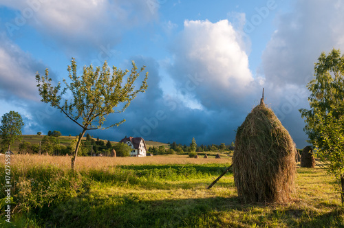 Rural landscape with haystacks in a summer sunny day. Rural mountain landscape with storm clouds. Thunderstom under field. House in the field of wheat. photo