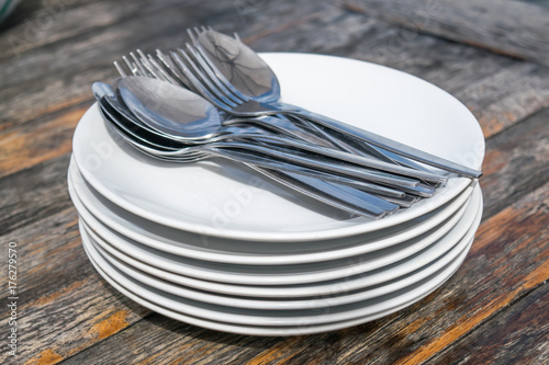 spoons and forks on stack of plates on wooden table - selective focus