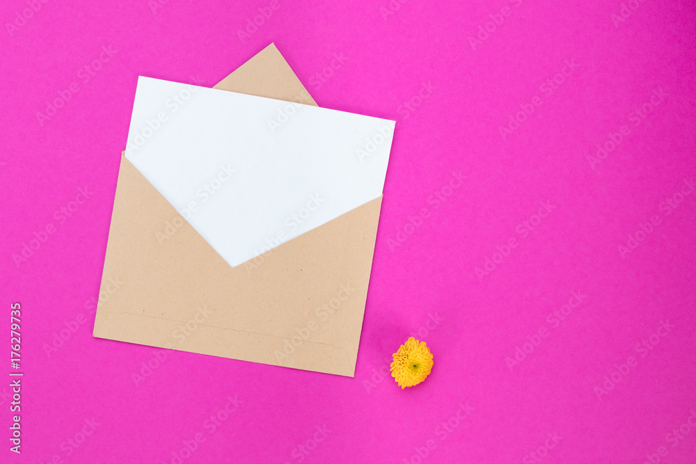 Pink background of a blank card with envelope and a little yellow flower. Copy space, view from above