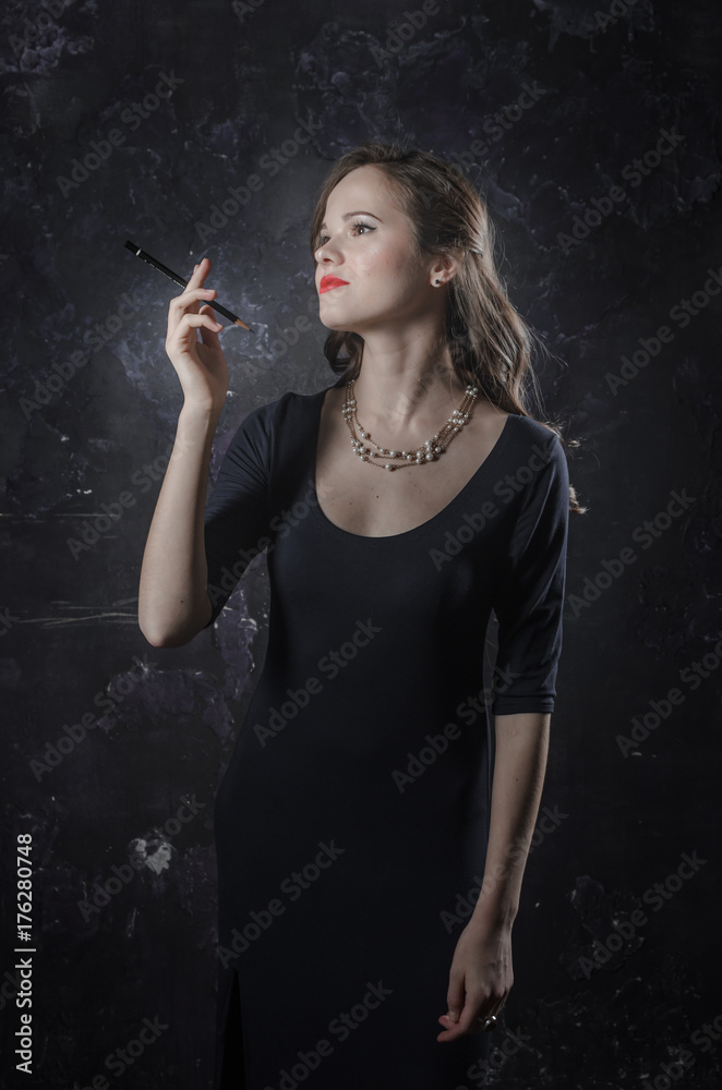 Fototapeta premium Girl in a reverie mood. Noir film style woman in dress holding black pen in her hand. Studio shot. Old fashion photo