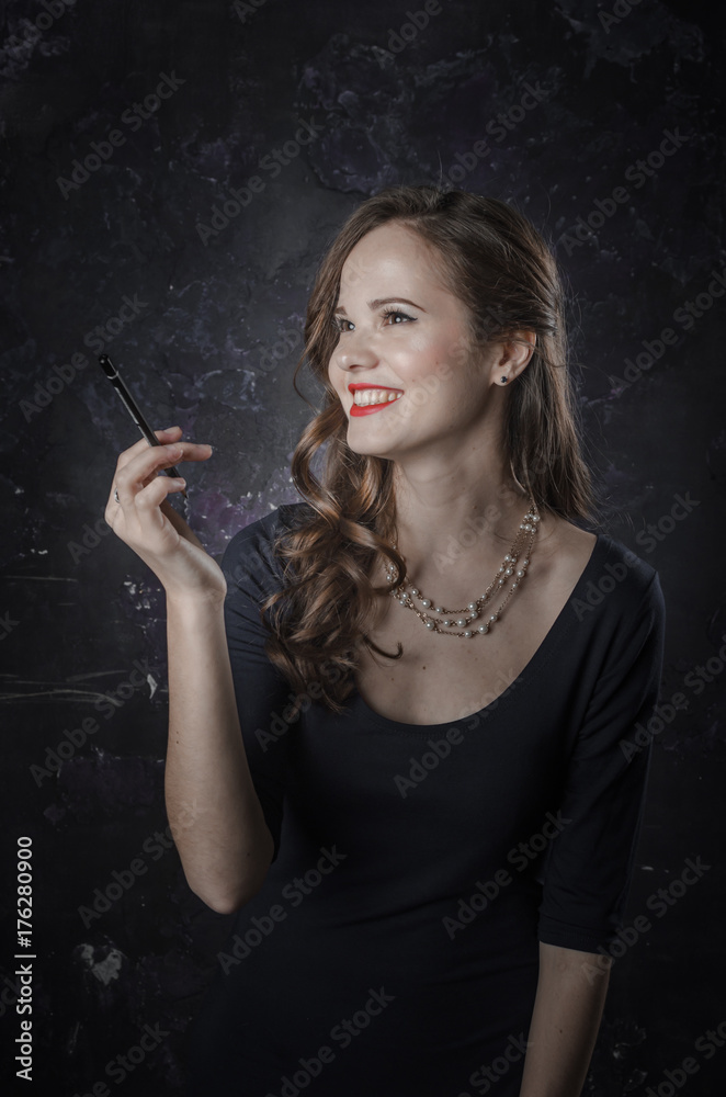 Obraz premium Female in a good mood and smiling. Noir film style woman in dress holding black pen. Studio shot. Old fashion photo