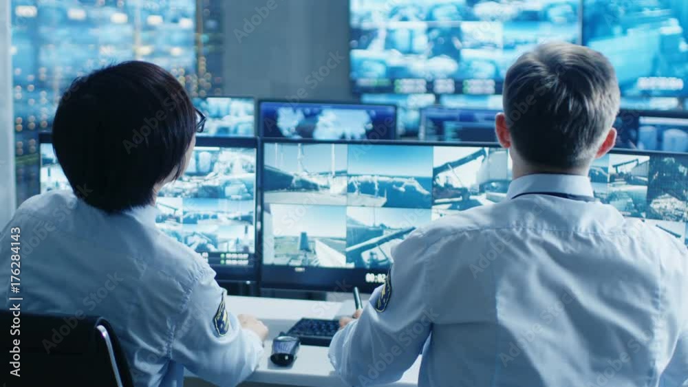 In the Security Control Room Two Officers Monitoring Multiple Screens for Suspicious Activities, They Report any Unauthorised Activities. They Guard Object of National Importance. In the Security Control Room Two Officers Monitoring Multiple Screens for Suspicious Activities, They Report any Unauthorised Activities. They Guard Object of National Importance.
