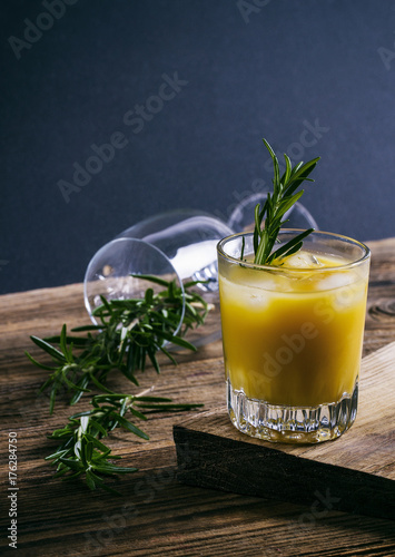 Orange alcoholic drink with rosemary and ice on wooden board