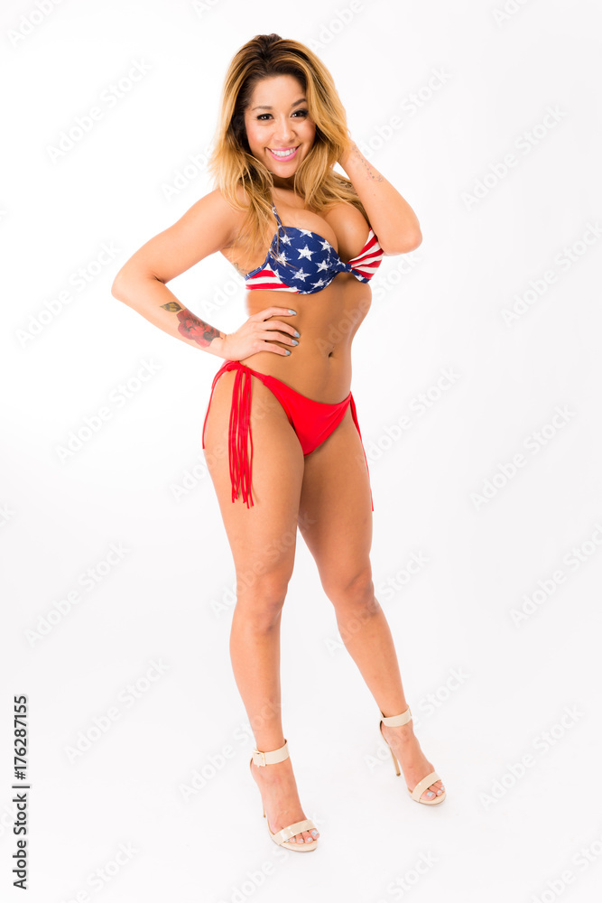Obraz premium Young fit hispanic woman in American Flag patterned swimsuit posing on a white background
