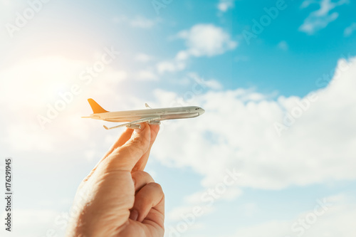 hand holding airplane model in front of cloudy blue sky background. air transportation concept.