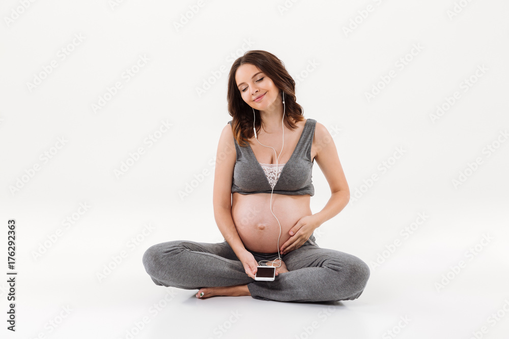 Pleased pregnant woman sitting on the floor while listening music