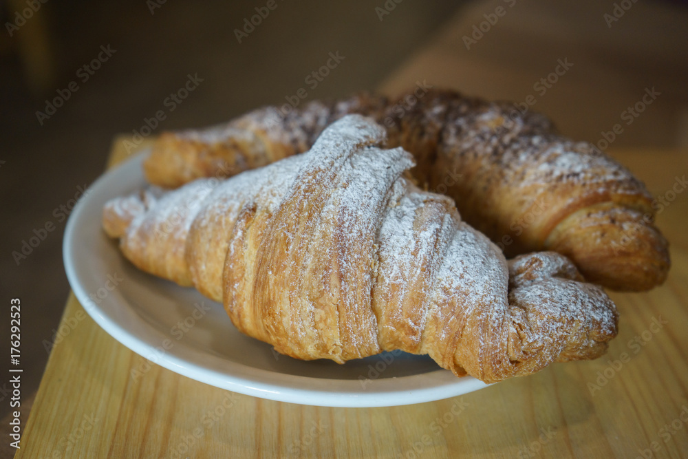 two croissants on a plate, sprinkled with powdered sugar two croissants on a plate, sprinkled with powdered sugar